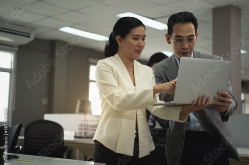 Businesswoman discuss with Businessman in office about job project both of them holding laptop lady point her finger to laptop explain job description to colleague and show to success in business plan