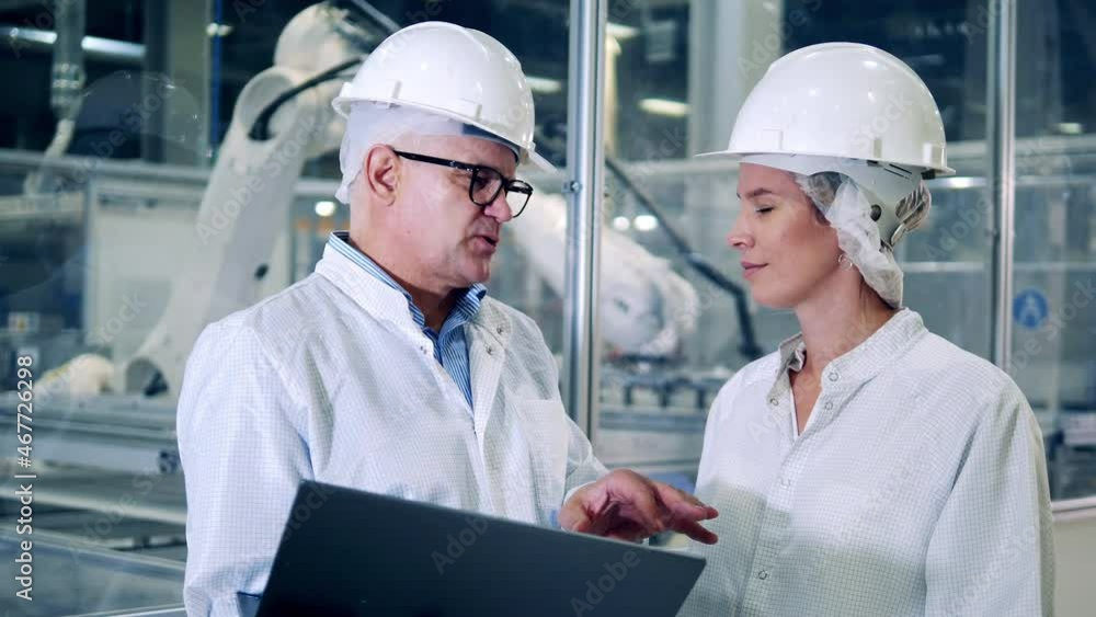Engineers, teamwork, modern factory facility. Two specialists in lab coats are talking at the solar cell factory