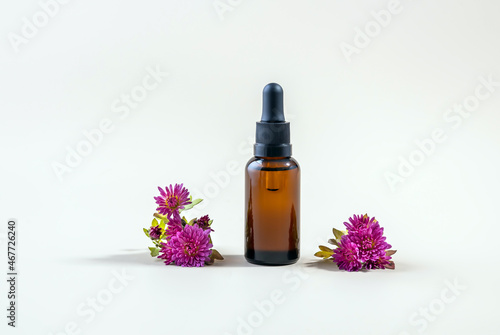 bottle of essential oil made of glass with a pipette and flowers on a light background. the concept of natural cosmetics