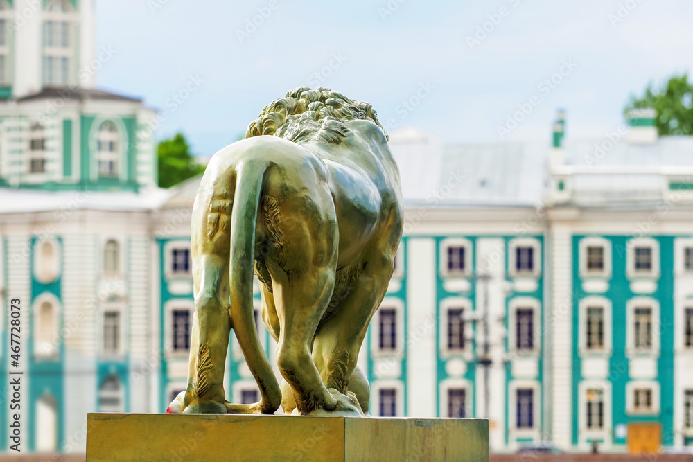 Saint Petersburg, Russia. Bronze lion at Dvortsovaya pier of the Admiralty Embankment Neva River, back view. Kunstkamera building as a background - obrazy, fototapety, plakaty 