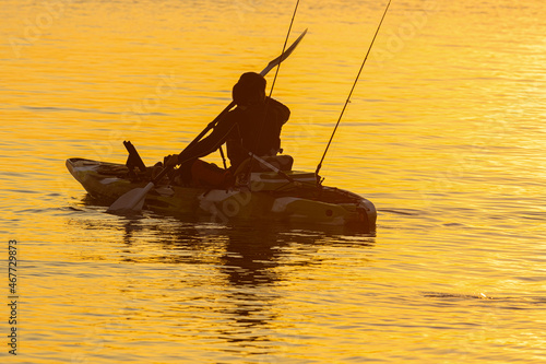 A woman is fishing on a small boat in the bright morning light.