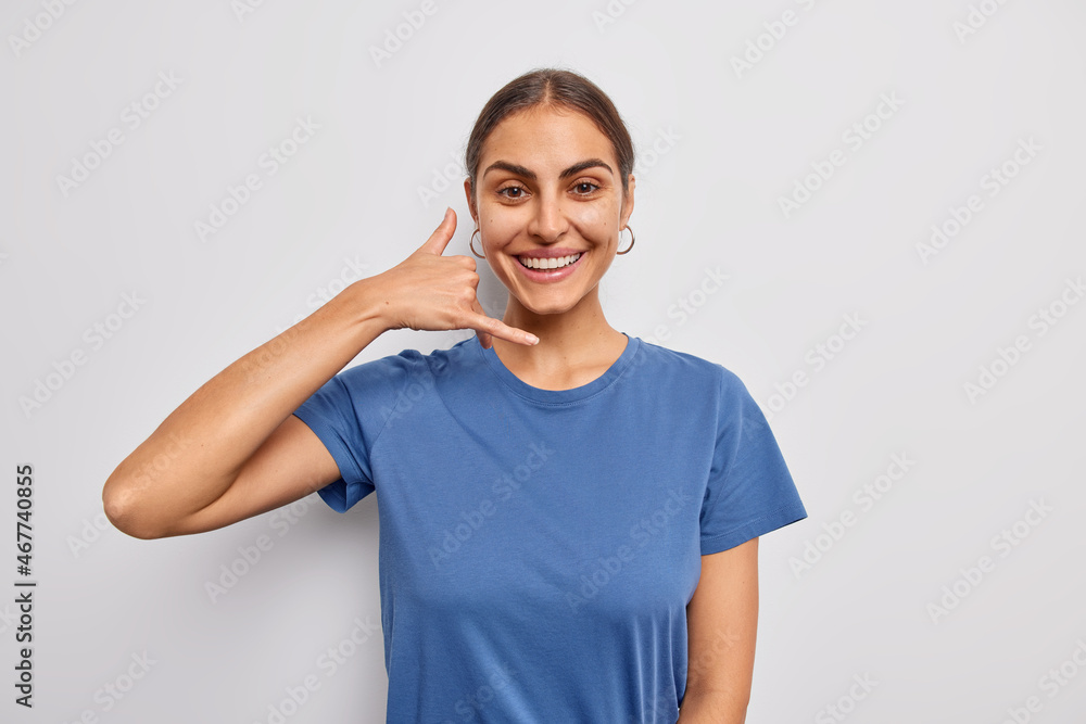 Waist up shot of pretty joyful woman makes call me gesture asks to contact her or meet next time dressed in casual blue t shirt isolated over white background. Body language and people concept Waist up shot of pretty joyful woman makes call me gesture asks to contact her or meet next time dressed in casual blue t shirt isolated over white background. Body language and people concept