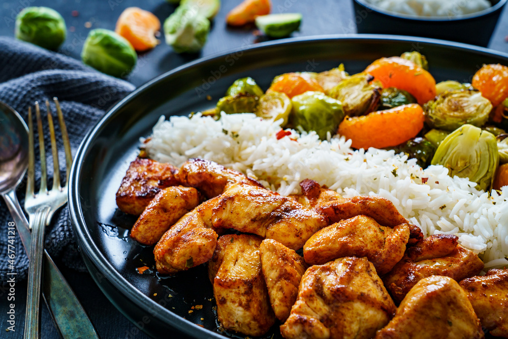 Fototapeta premium Fried chicken nuggets with white rice, brussels sprouts, carrots and tangerines on wooden table 