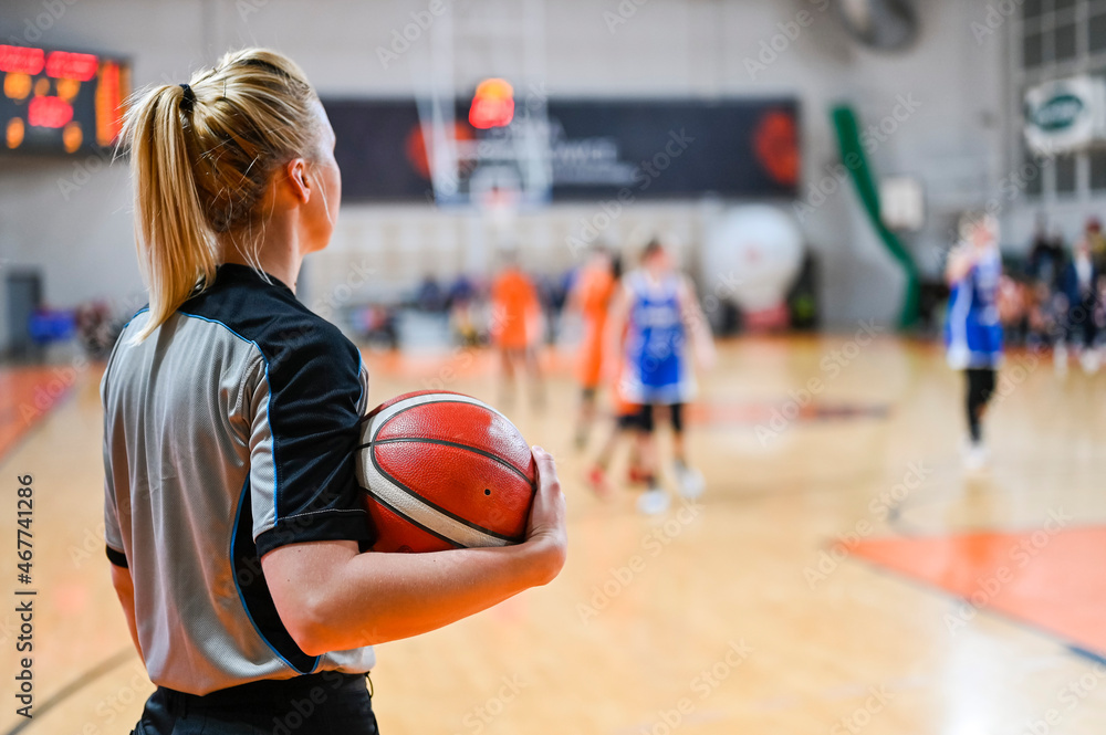 Woman referee keeps the ball during basketball match.