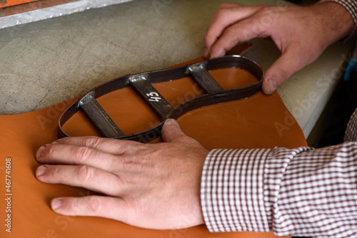 Shoemaker hands putting steel form on leather to make shoe insole on cutting machine in workshop. Leather crafting handmade shoes. Selective focus.
