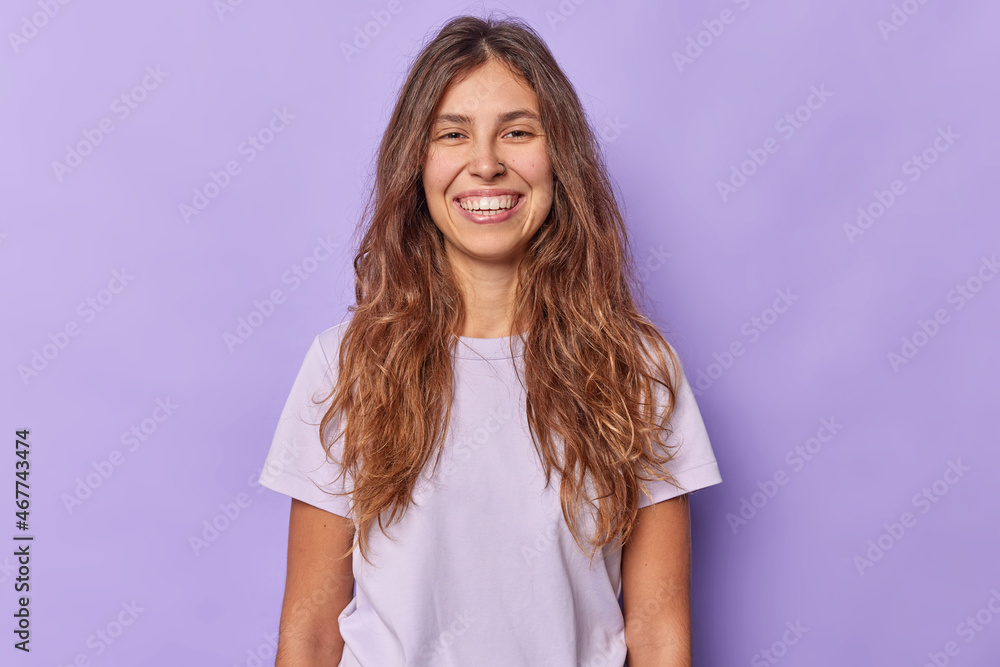 Horizontal shot of happy positive young woman with toothy smile poses against purple background in casual clothes glad to receive compliment from boyfriend has piercing in nose. Emotions concept Horizontal shot of happy positive young woman with toothy smile poses against purple background in casual clothes glad to receive compliment from boyfriend has piercing in nose. Emotions concept