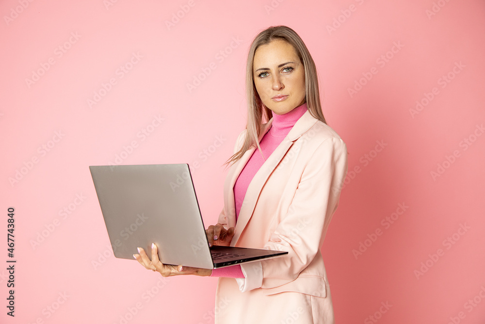 Beautiful businesswoman standing and holding laptop computer oh hands looking at camera on pink background in studio, business people concept Beautiful businesswoman standing and holding laptop computer oh hands looking at camera on pink background in studio, business people concept