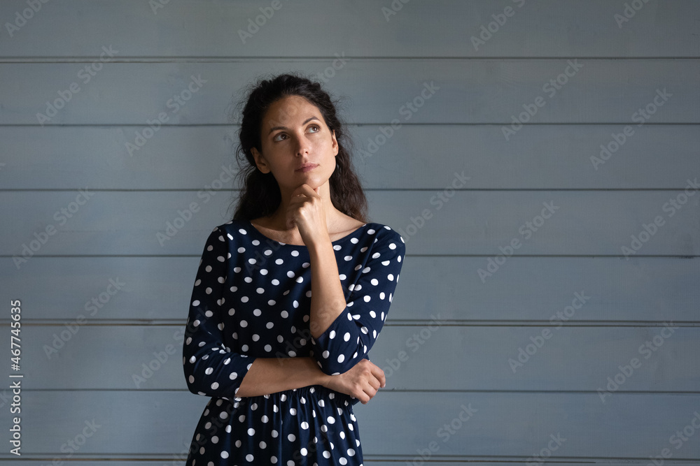 Thoughtful young latin woman stand close to grey wall look up ponder on interesting offer proposal imagine result. Puzzled millennial lady touch chin reflect on idea make choice decision. Copy space Thoughtful young latin woman stand close to grey wall look up ponder on interesting offer proposal imagine result. Puzzled millennial lady touch chin reflect on idea make choice decision. Copy space