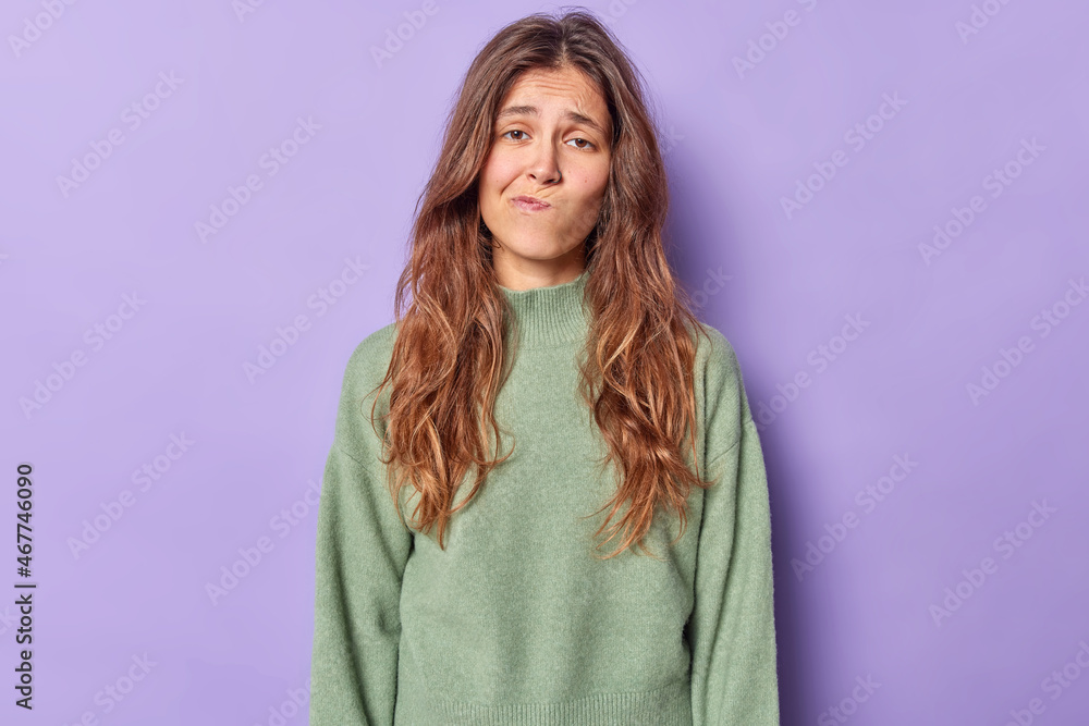 Studio shot of displeased bored woman purses lips and looks with uninterested expression wears casual jumper poses alone against purple background. Upset gloomy teenage girl tired of distance studying Studio shot of displeased bored woman purses lips and looks with uninterested expression wears casual jumper poses alone against purple background. Upset gloomy teenage girl tired of distance studying