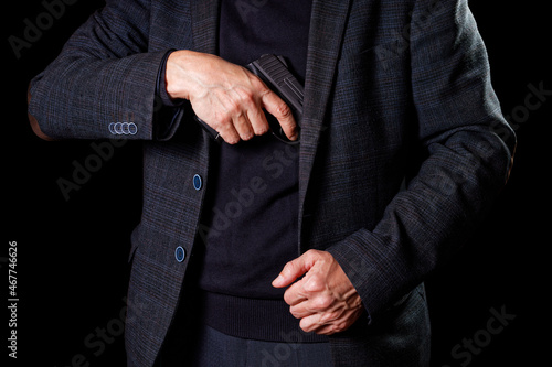 A man in a suit takes out a pistol from a jacket in darkness.