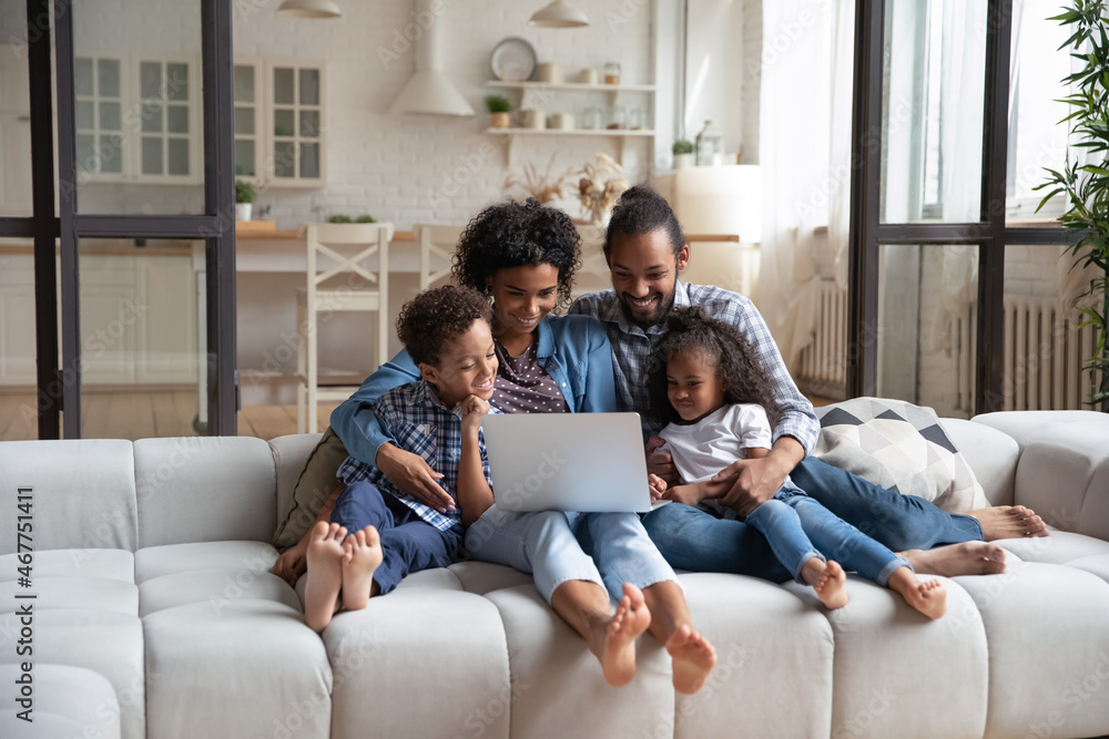 Happy African American family enjoying leisure time at laptop, resting on couch, watching movie together. Millennial couple of parents and sibling kids relaxing at home, making video call Happy African American family enjoying leisure time at laptop, resting on couch, watching movie together. Millennial couple of parents and sibling kids relaxing at home, making video call