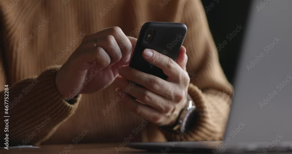 Close up shot of man hands with watch using mobile phone while working at laptop. Male fingers typing and tapping on smartphone. Texting and scrolling. Slow motion.