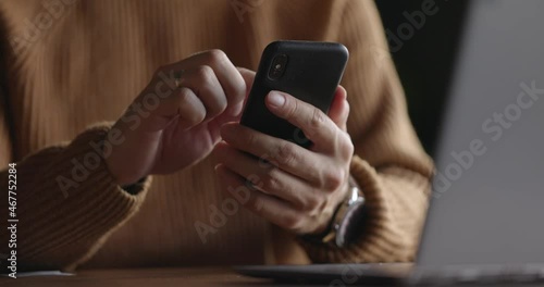 Close up shot of man hands with watch using mobile phone while working at laptop. Male fingers typing and tapping on smartphone. Texting and scrolling. Slow motion.