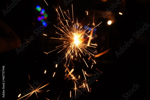 Sparkler on fire with black background and bokeh Diwali lights.