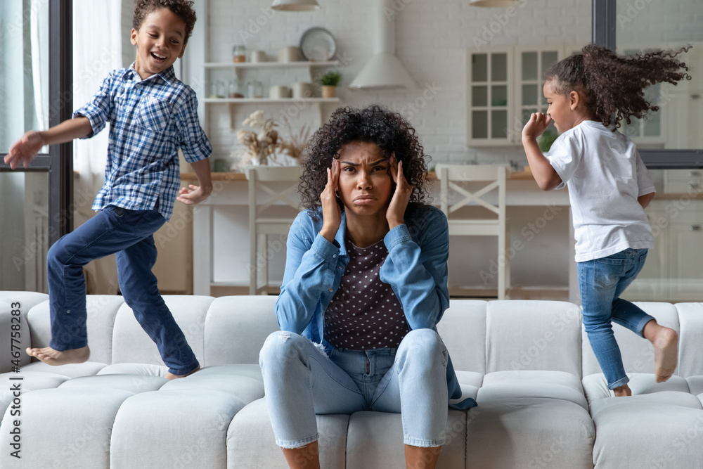 Naught Mom Fotka „Excited naughty, noisy African children running around mom on sofa, shouting, making mother upset, annoyed. Frustrated mum sitting on couch at home, feeling headache, stress. Parenting problems“ ze služby Stock |
