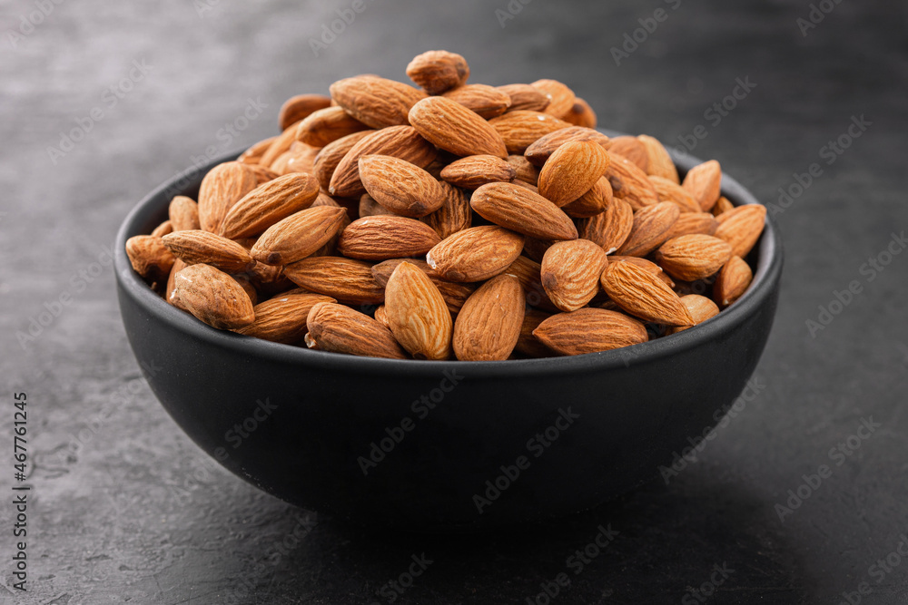 Peeled almonds in a bowl on a black textured background, side view. Peeled almonds in a bowl on a black textured background, side view.