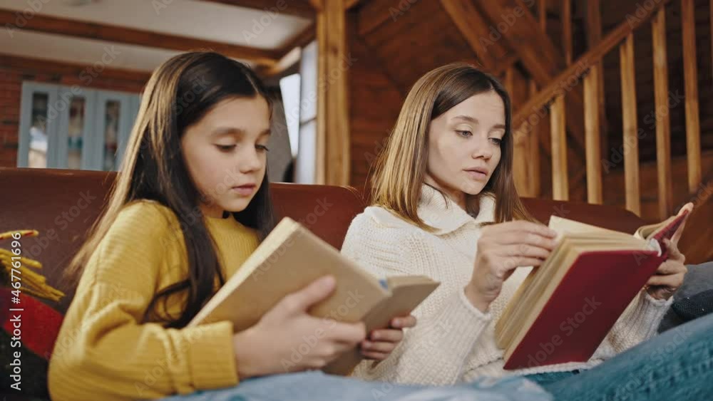 Young mother and little daughter reading books while sitting on couch in cozy kitchen of wooden country house. Close up Young mother and little daughter reading books while sitting on couch in cozy kitchen of wooden country house. Close up