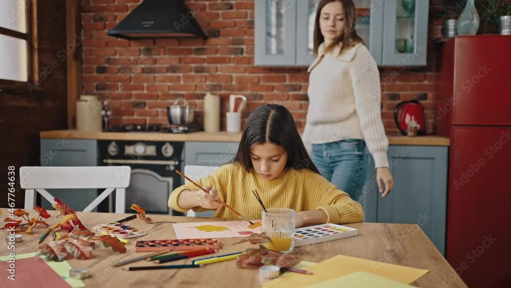 Preteen daughter drawing autumn leaves, sitting at table in kitchen at home. Her mom coming up, sitting down nearby, smiling – Stock-Video | Adobe Stock 