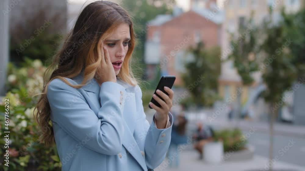 Business woman caucasian girl lady female looking in mobile phone feels shock upset worries about bad news problems of refusal financial notification mistake holds head with hand from stress in city Business woman caucasian girl lady female looking in mobile phone feels shock upset worries about bad news problems of refusal financial notification mistake holds head with hand from stress in city