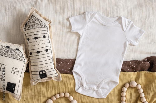 Styled stock photo of clear white baby onesie with scandinavian stitched pillow in the shape of a house and wooden toys on yellow napkin for creating mockup for presentation kids sublimation design