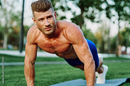 athletic man with pumped up muscular body in the park doing exercise