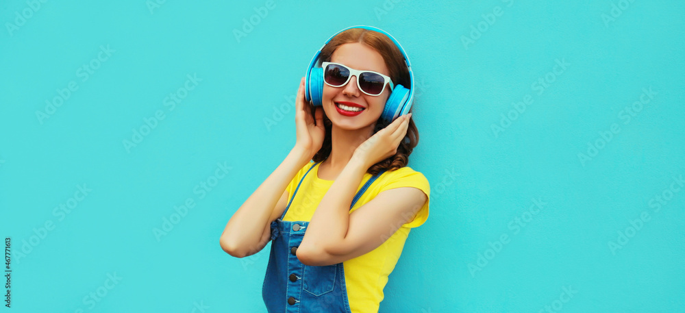 Portrait of happy smiling young woman with headphones listening to music on a colorful blue background Portrait of happy smiling young woman with headphones listening to music on a colorful blue background