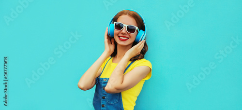 Portrait of happy smiling young woman with headphones listening to music on a colorful blue background