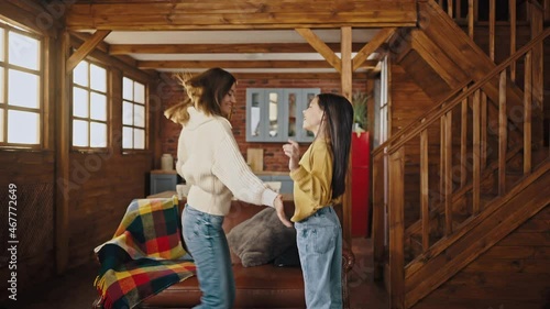 Young mum and little daughter laughing, dancing, whirling and tickling while having fun in kitchen of wooden country house. Slow motion