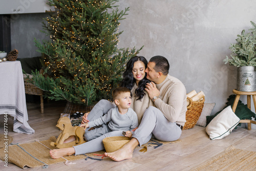 A stylish young beautiful family with a young son is playing on the floor near the Christmas tree in the living room © Sunshine