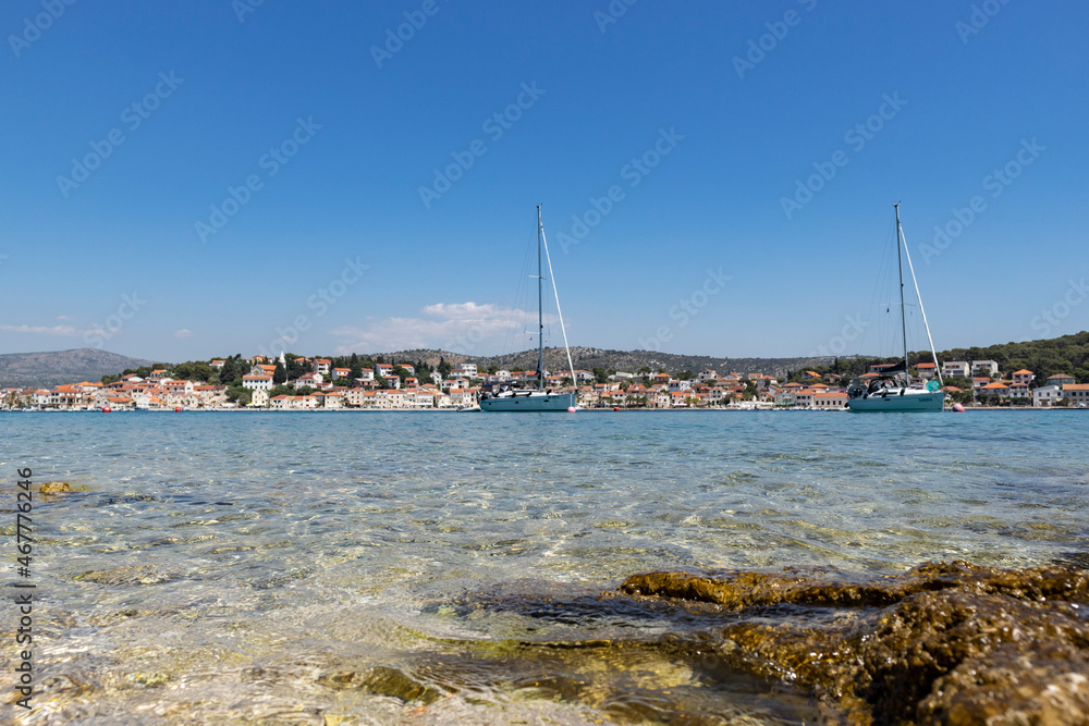White sailing boats anchored in front of small fishing town of Rogoznica, Croatia on the coast of Adriatic sea White sailing boats anchored in front of small fishing town of Rogoznica, Croatia on the coast of Adriatic sea