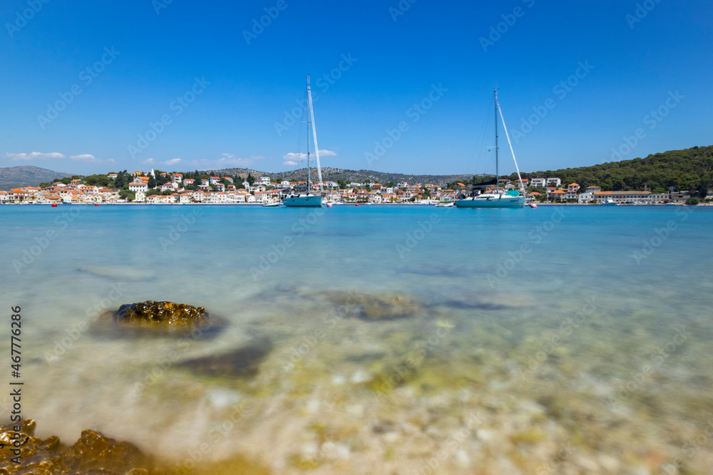 White sailing boats anchored in front of small fishing town of Rogoznica, Croatia on the coast of Adriatic sea