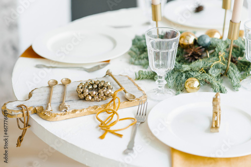 Christmas decor of the festive table for dinner. Golden wreath of bells on a beautiful cutting board and cutlery