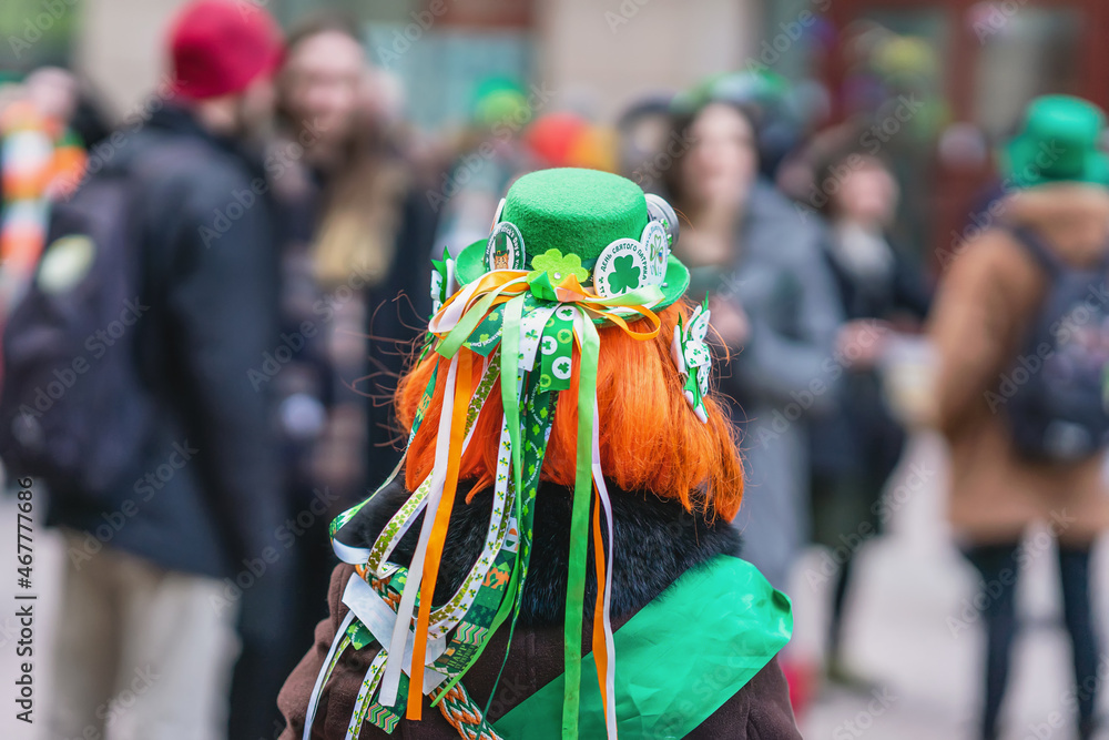 Back view of girl with red hair in hat with decorations, symbols of St. Patrick's Day, parade in city