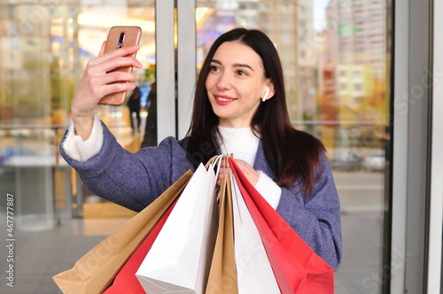 Young brunette woman with shopping bags makes a video call outside 