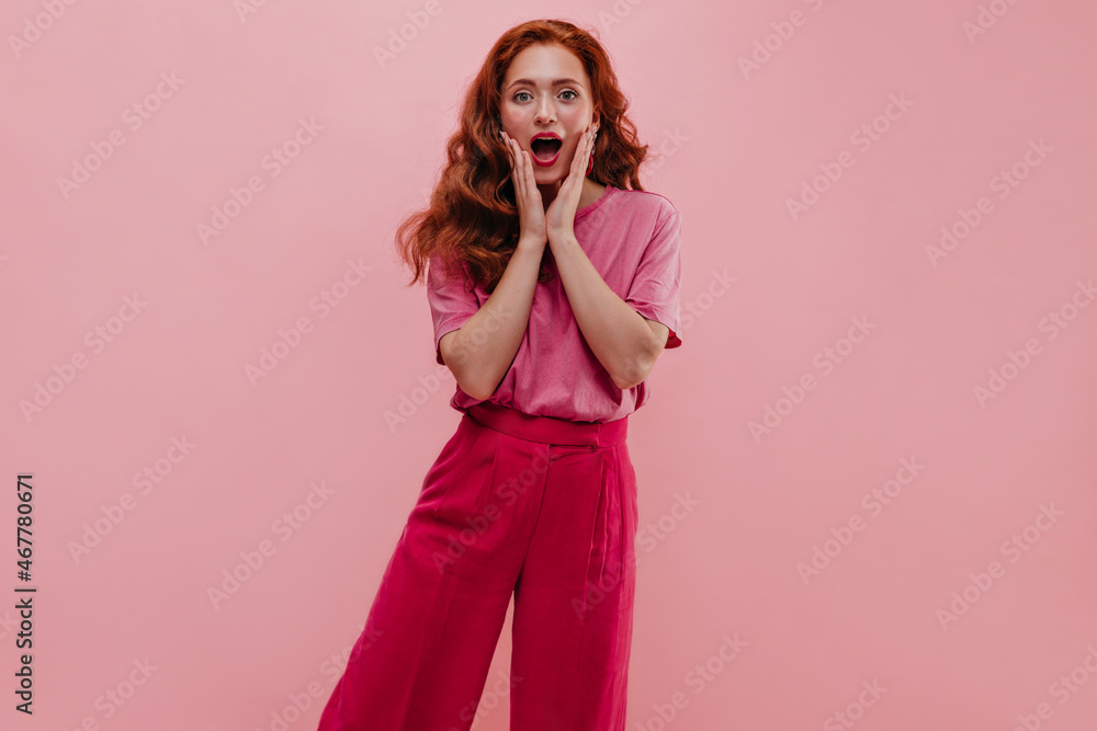 Redhead caucasian lady looking at camera with mouth wide open on pink background. Teenager holding hands on cheeks with shocking expression in casual clothes. Reaction to unpleasant situation, concept Redhead caucasian lady looking at camera with mouth wide open on pink background. Teenager holding hands on cheeks with shocking expression in casual clothes. Reaction to unpleasant situation, concept
