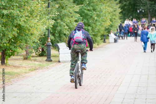 A man on a bicycle in a park where many people are walking.