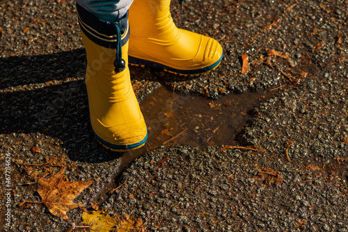 Child with rubber rain boots walking on wet sidewalk in autumn afternoon