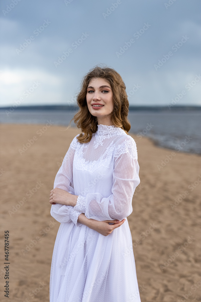 Happy young girl in a white dress on the river bank. Stormy sky over the river Happy young girl in a white dress on the river bank. Stormy sky over the river