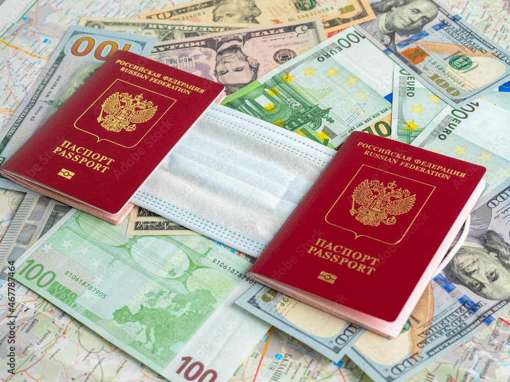 Two Russian passports are on dollar and euro bills. A medical mask is attached between the passports. The concept of traveling during a pandemic and diseases Two Russian passports are on dollar and euro bills. A medical mask is attached between the passports. The concept of traveling during a pandemic and diseases