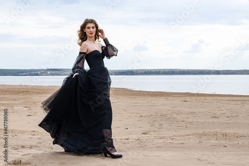 Happy young girl in black dress on the river bank