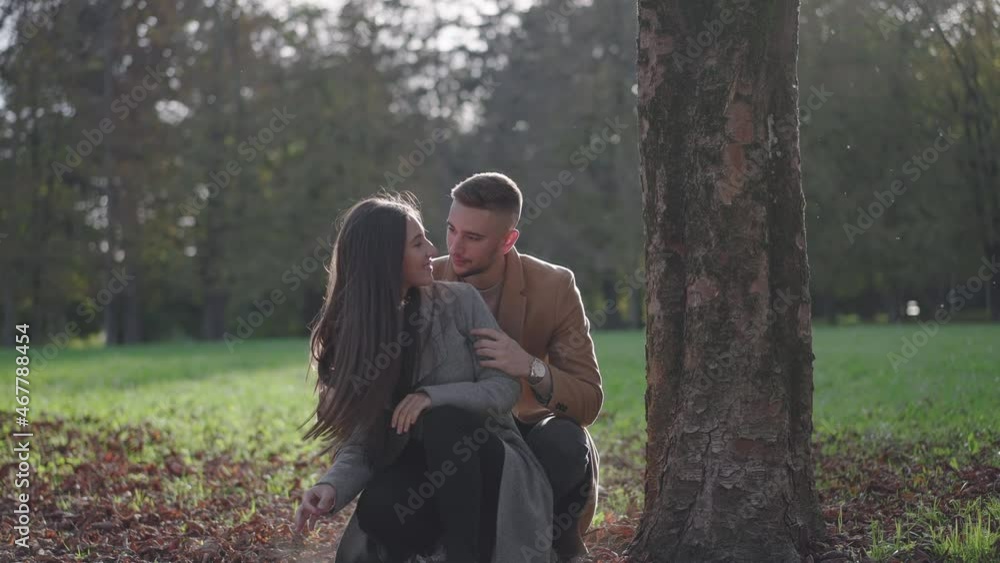 Slow motion – Young woman kneeling in the park while her boyfriend surprises her with the hug from behind. Young couple meeting in the park Slow motion – Young woman kneeling in the park while her boyfriend surprises her with the hug from behind. Young couple meeting in the park