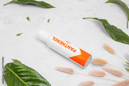 Aerosol of panthenol on a white background with green leaves. Protection against burns, diaper rash, wound healing spray