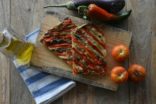 Coca de recapte typical catalan food similar to pizza with vegetables in a wooden table and some vegetables around photo