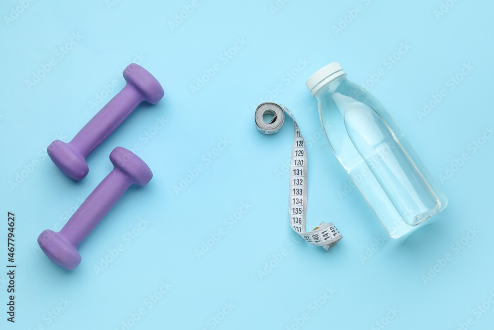 Dumbbells, measuring tape and bottle of water on blue background Dumbbells, measuring tape and bottle of water on blue background