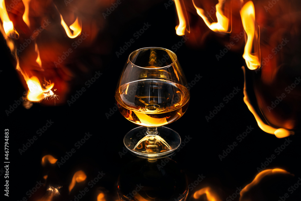 Glass with whiskey with fire and reflections on black background