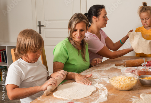 Two middle-aged women with little children are making pizza