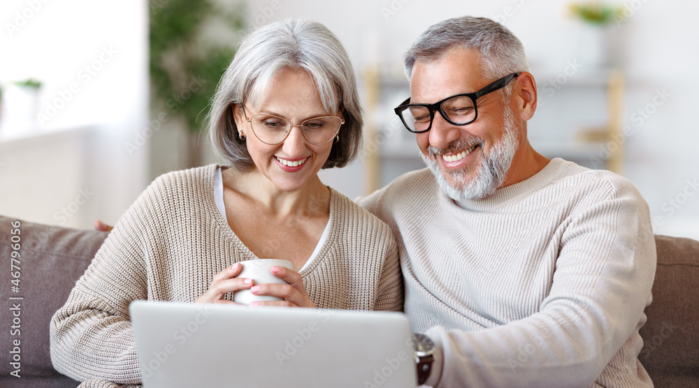 Fototapeta premium Happy senior family couple watching comedy or funny video on laptop while spending free time at home