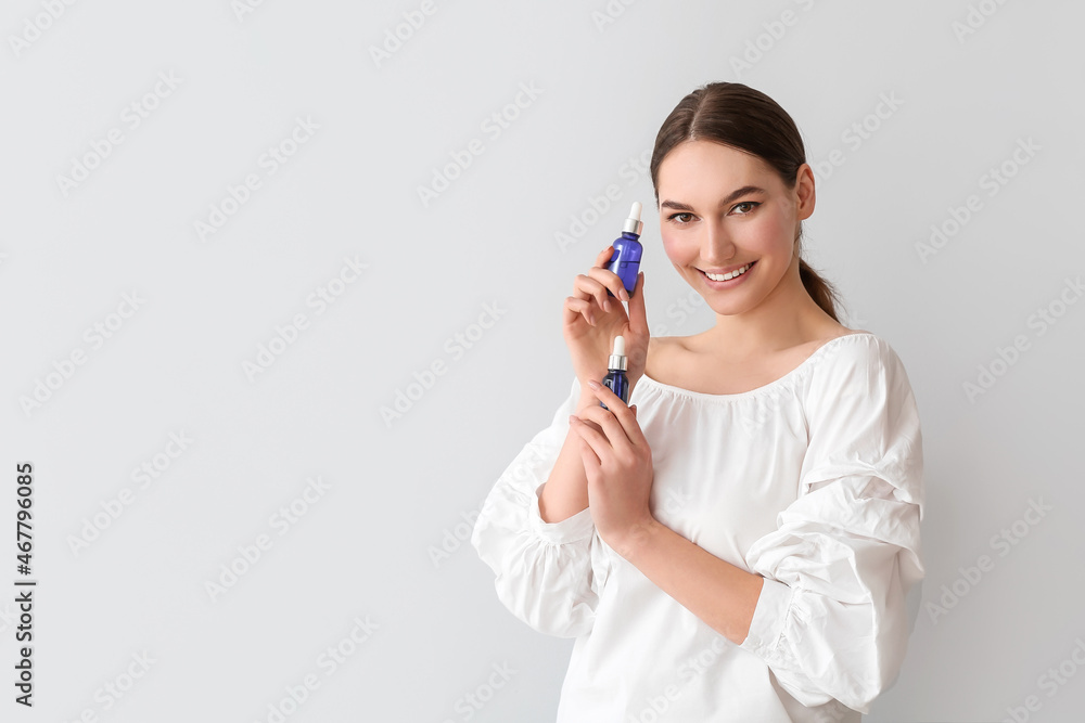 Smiling woman holding bottles of essential oil on light background Smiling woman holding bottles of essential oil on light background