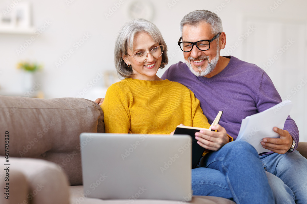 Happy senior couple reading good news in letter while paying bills online on laptop