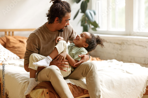 Happy afro american family father and son laughing and playing while sitting on bed at home photo